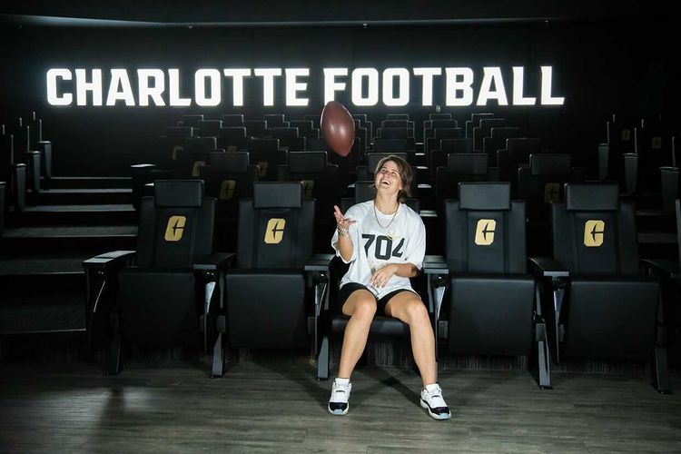 woman sitting in stadium chair with neon "Charlotte Football" above her