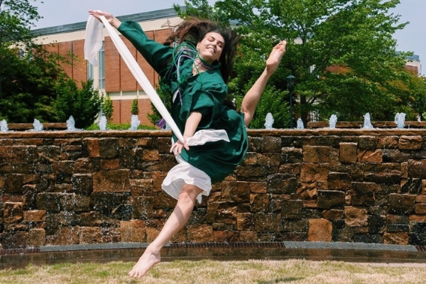 photo of recent graduate in cap and gown doing a dance jump 