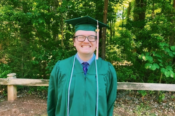 photo of recent graduate in cap and gown in front of trees