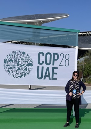 Liz McCormick in Dubai in front og COP 28 banner