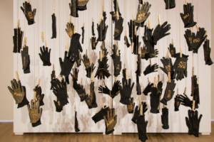 art piece of black gloves covered in paint hanging against a white wall