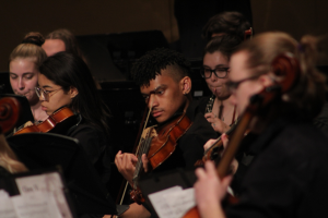 Student playing the violin with the orchestra on stage 