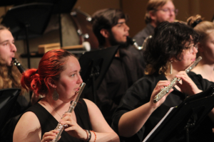 Student playing flute surrounded by other students playing wind instruments on stage