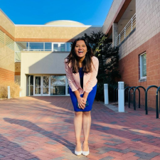 Lochana in a blue dress and pink jacket in front of the architecture building