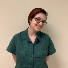 Sydney standing in front of a brown wall in a green shirt while smiling