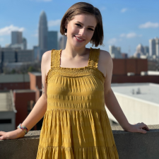 Sarah standing in front of a city skyline in a yellow dress
