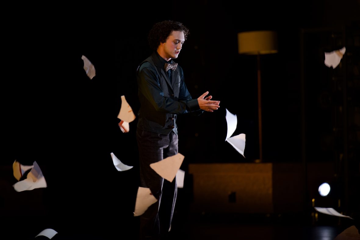 Theatre student on a dark stage with papers flying