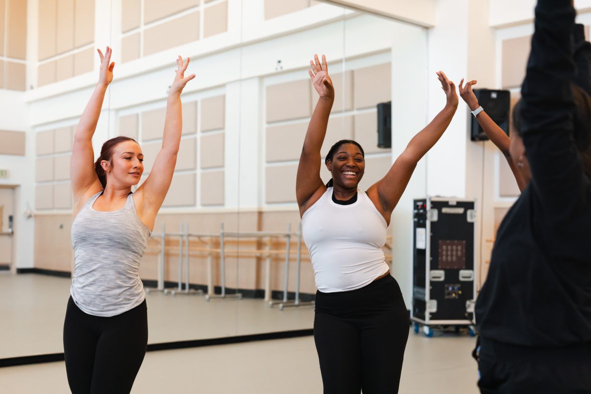 Two dance students with their hands above their heads in a jazz motion in the studio