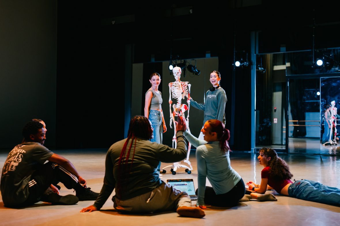 Dance students in the studio practicing anatomy with a skeleton in the center