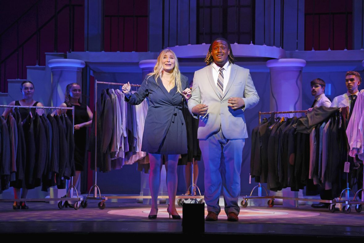 A woman and man on stage, the main characters of Legally Blonde, wearing suits