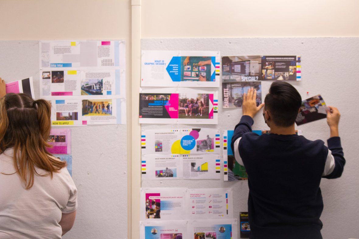 student pinning up graphic design presentation to poster board