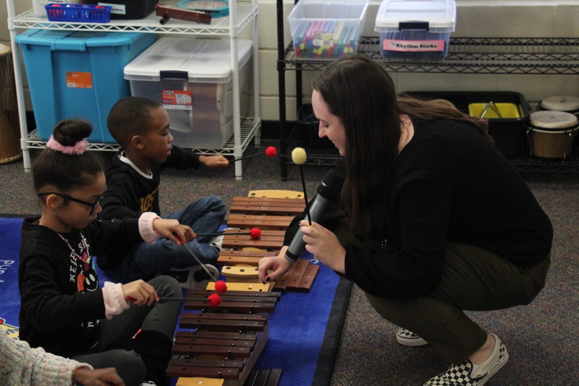 Music ed student teaching two young students how to play a children's instrument