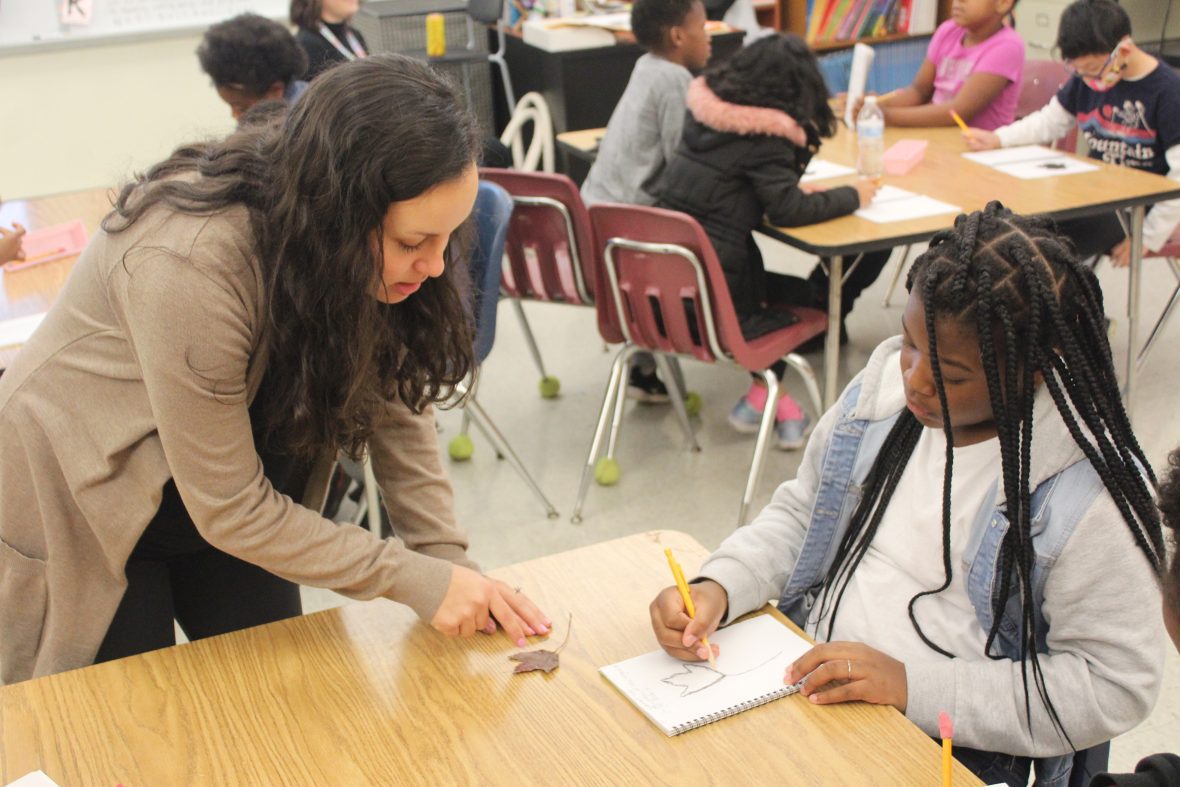 student working with an elementary school student on her drawing