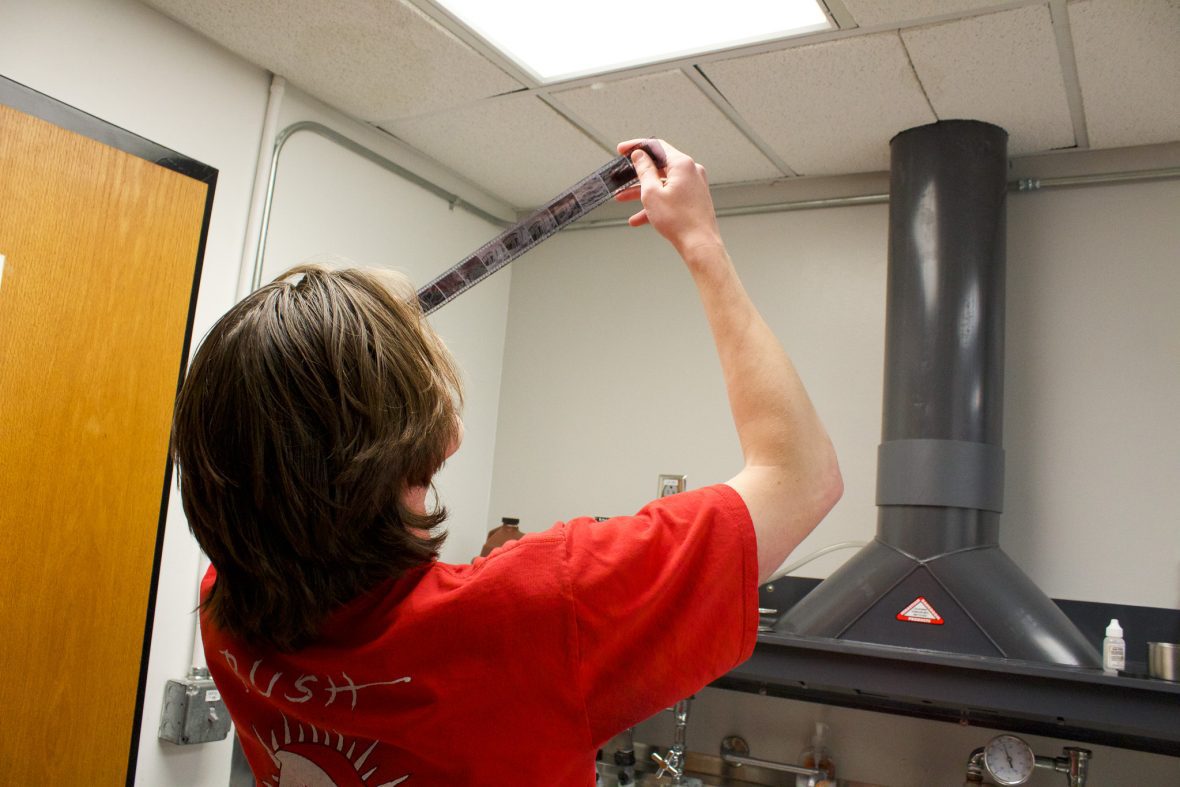 student holding up film strip in the dark room