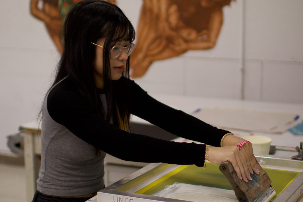 female student working with the print machine in the studio