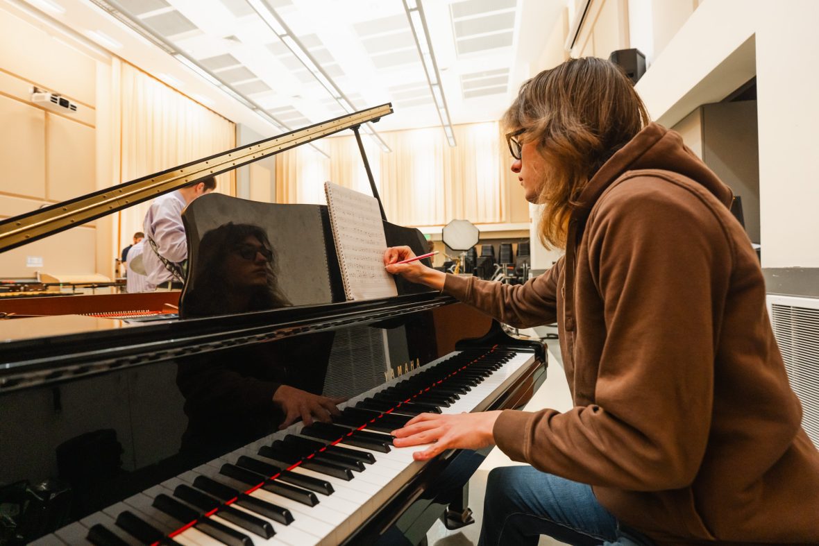 Student at the piano in a classroom writing down notes in composition notebook