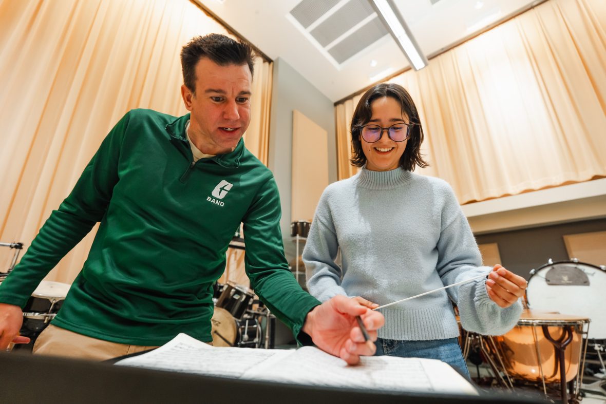 A professor teaching a student in a classroom, holding conducting wand