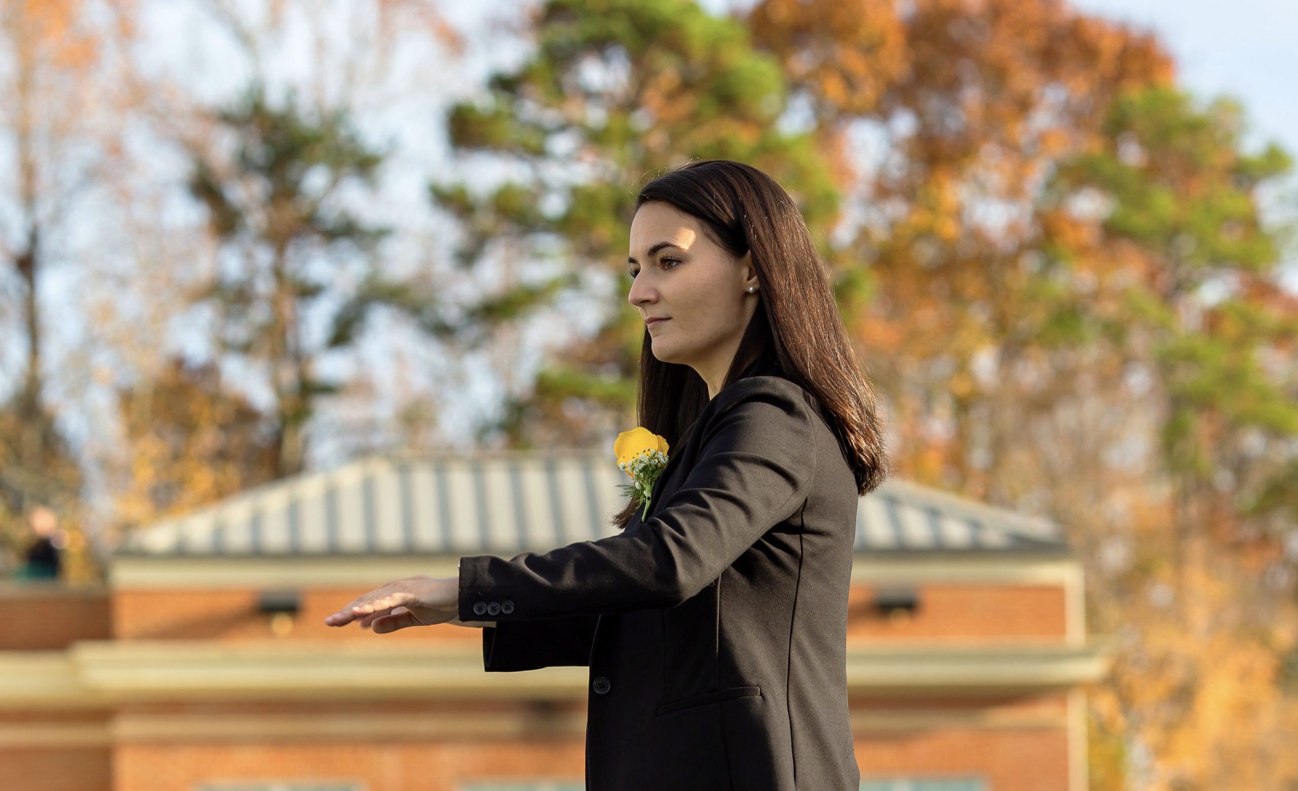 Alumni Emily Golden standing outside with fall leaves and conducting students