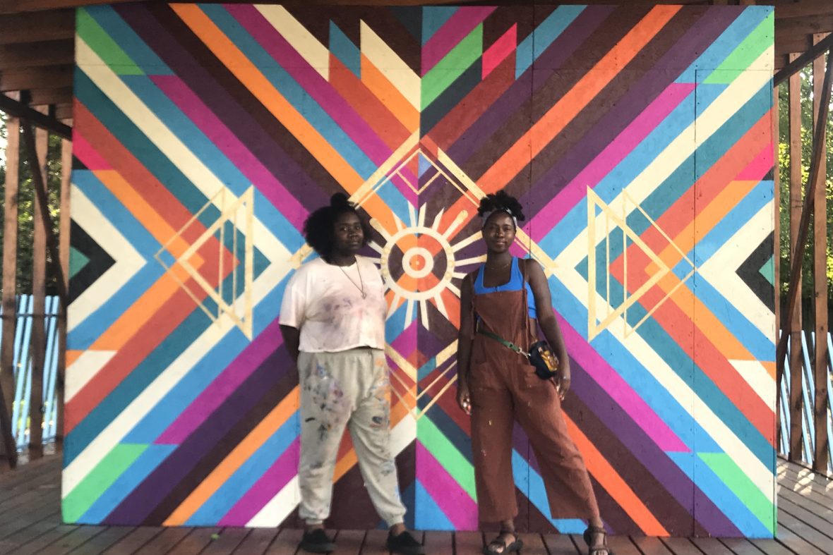 Student and alumna standing in front of a wall mural they designed