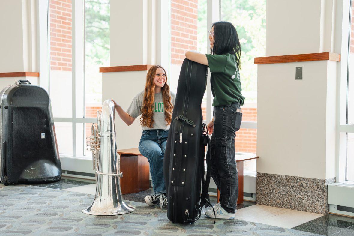 Two music students, one sitting down in Robinson Hall, holding their instruments