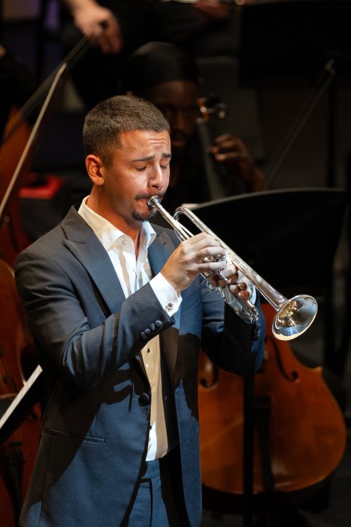 male student with trumpet playing on stage with the orchestra