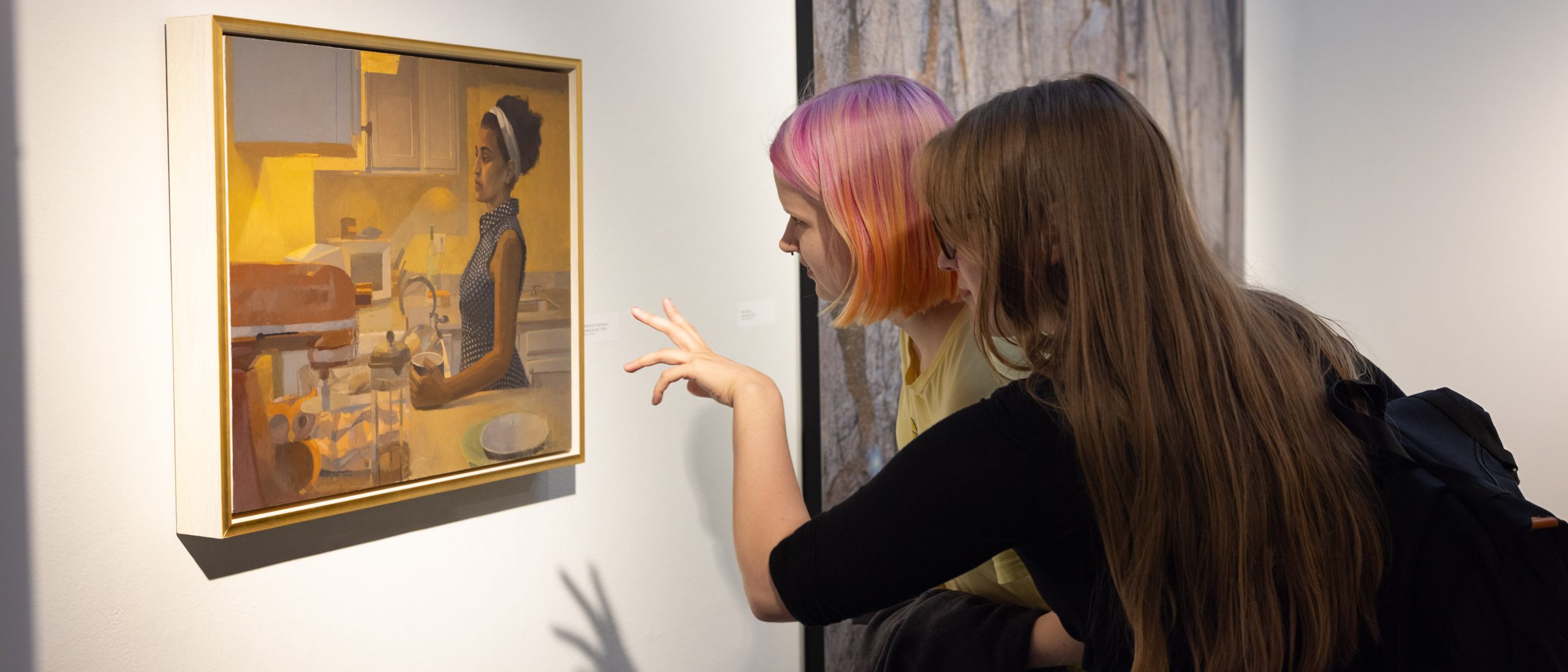 Two students pointing and assessing a painting on the wall