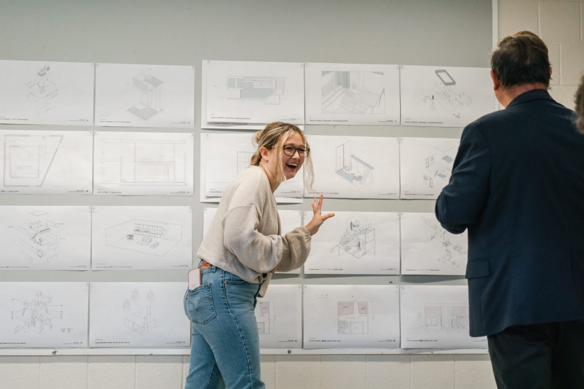 student laughing with professor in front of project pinned up to a grey wall