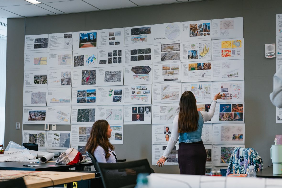 two female architecture students pinning up their project to a wall