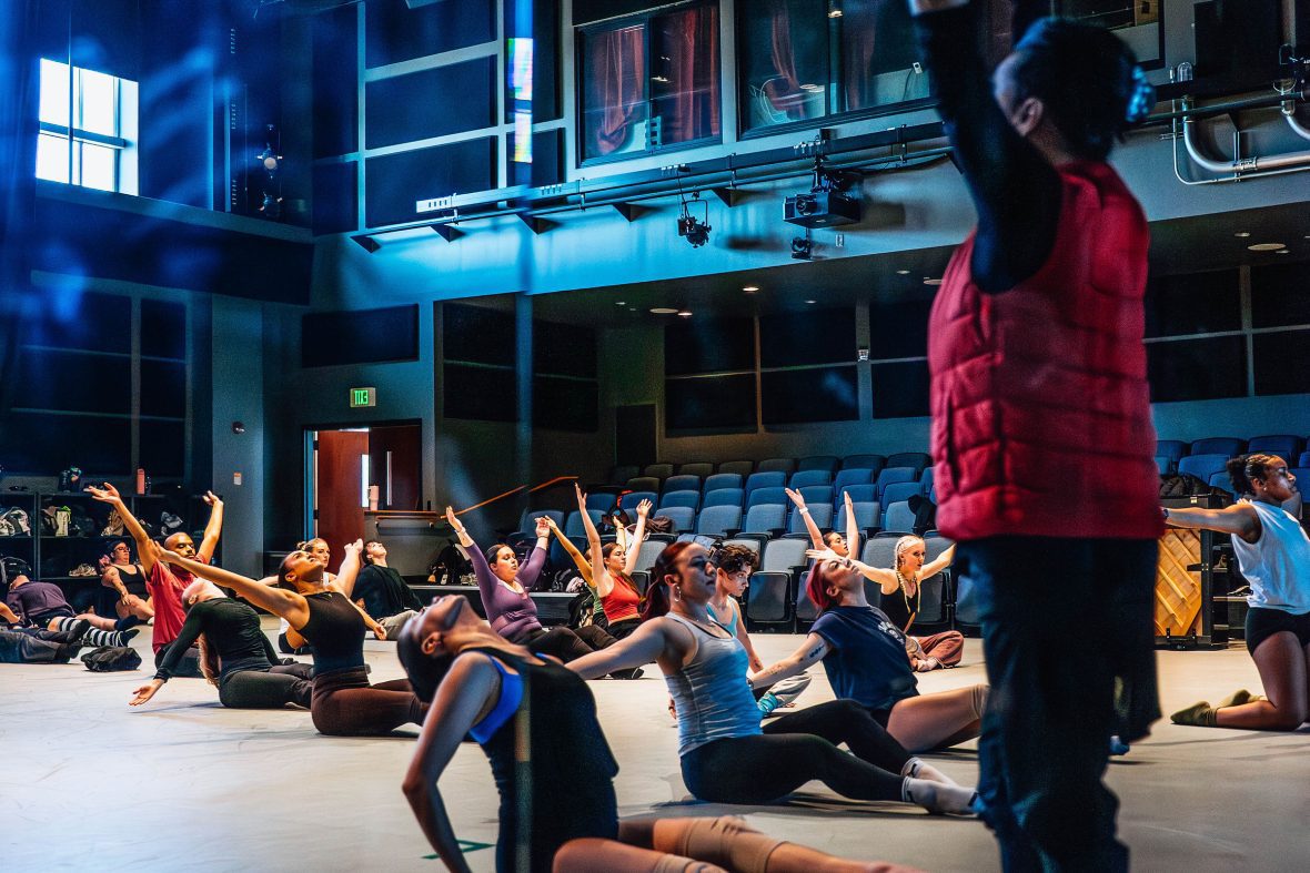 Modern class with students sitting on the floor with professor in front of them in red vest