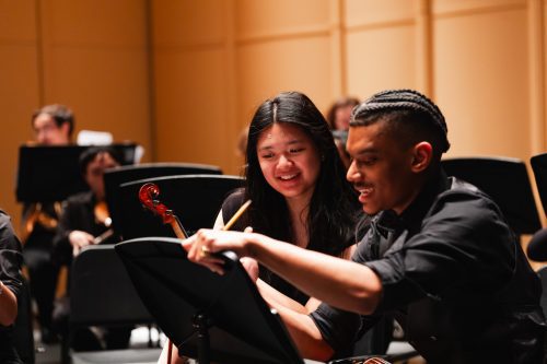 Two students laughing and looking at a music sheet