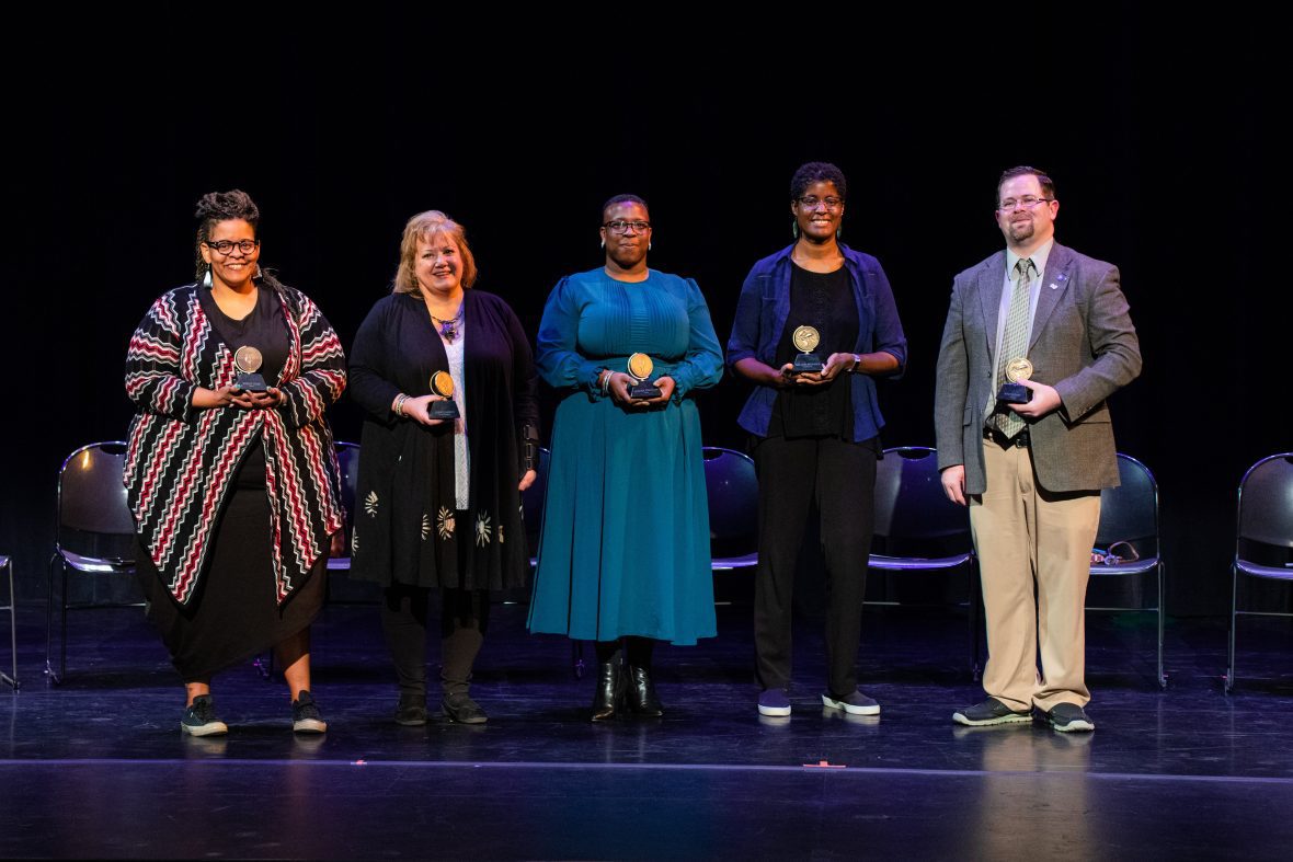 five alumni with their awards on stage