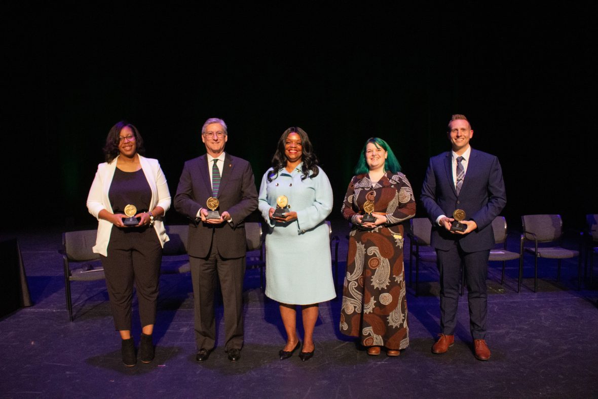 five alumni standing on stage holding awards