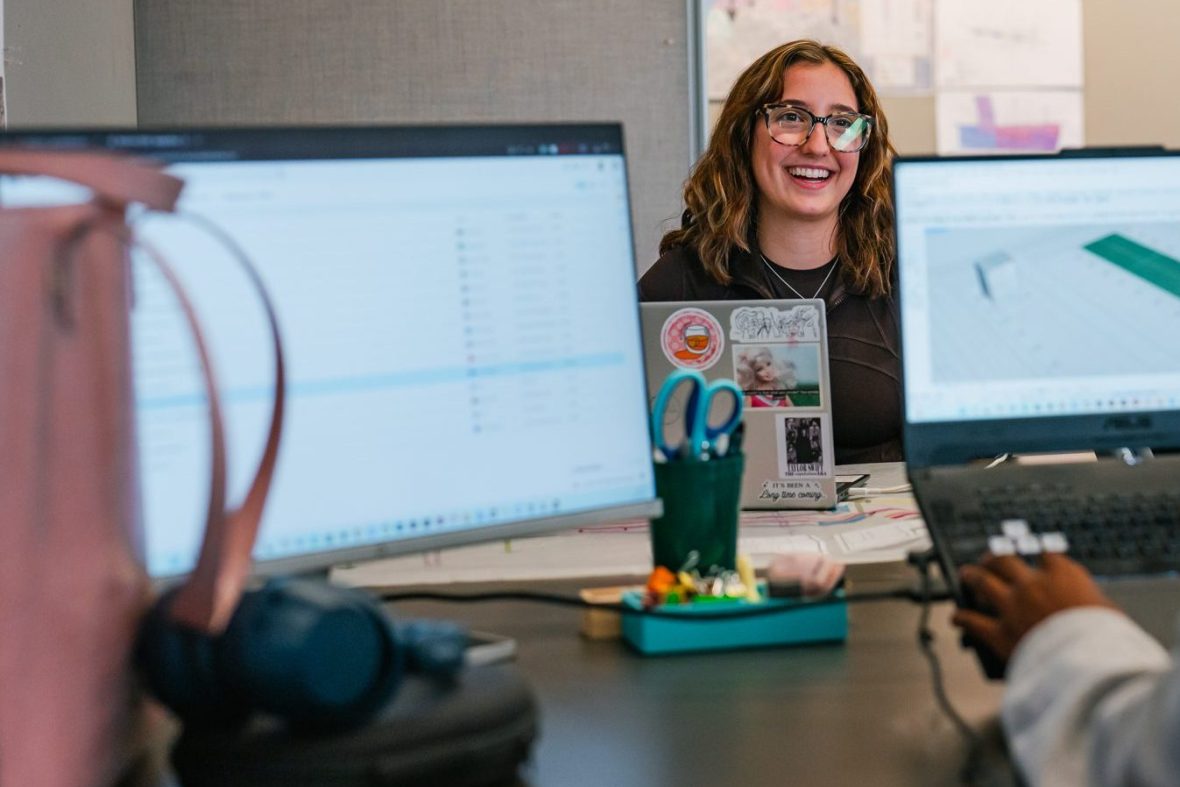 Student behind two laptops, smiling