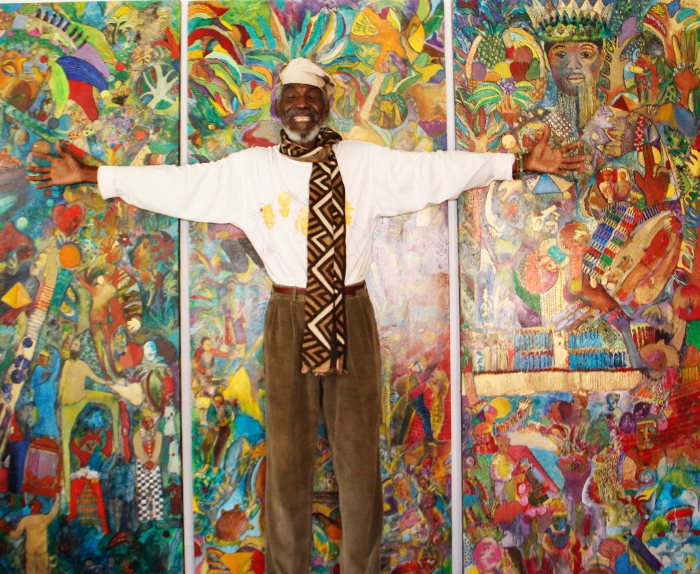 Man standing with arms outstretched in front of brightly colored paintings