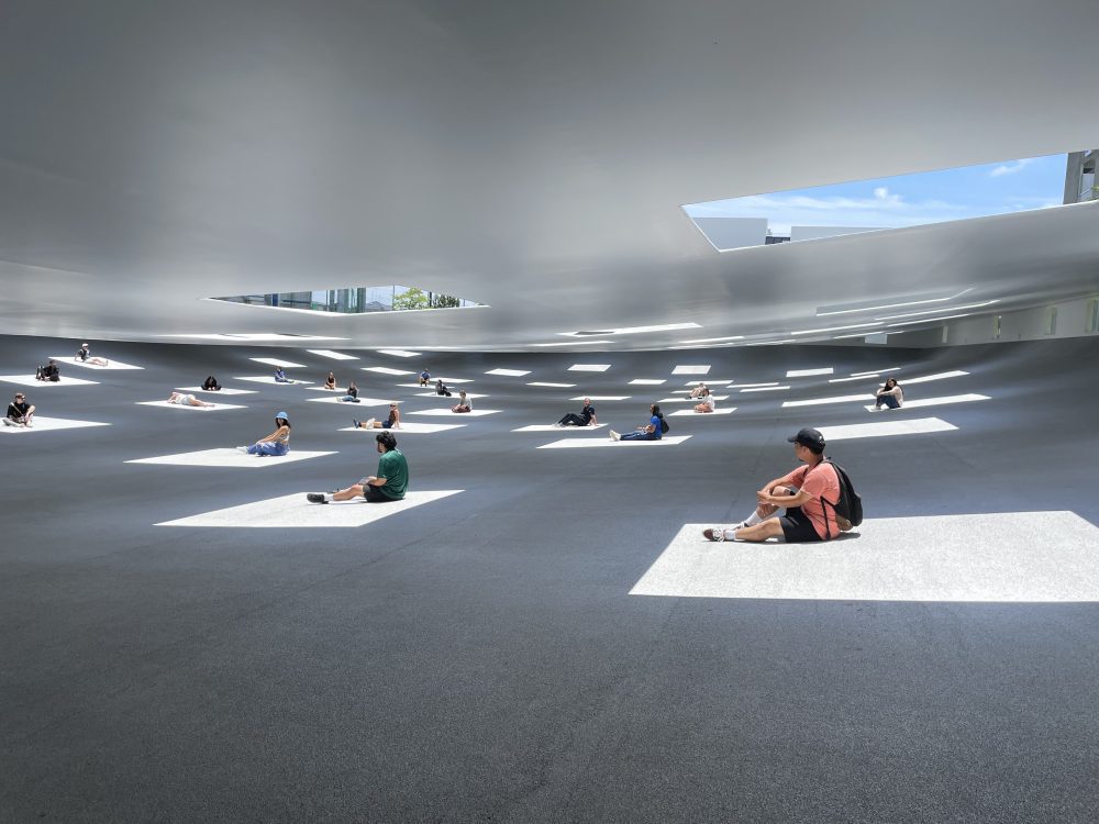 Students sitting under a large white roof inside squares the sun is casting
