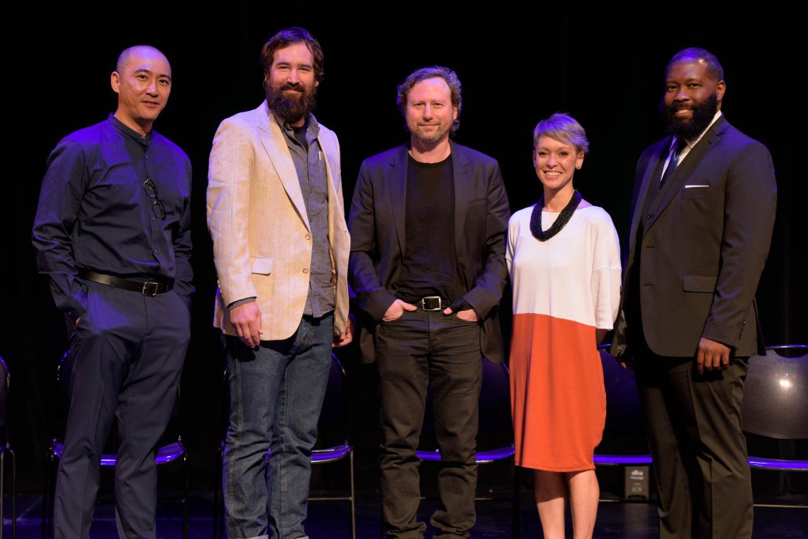 five alumni standing on stage with blue stage lighting