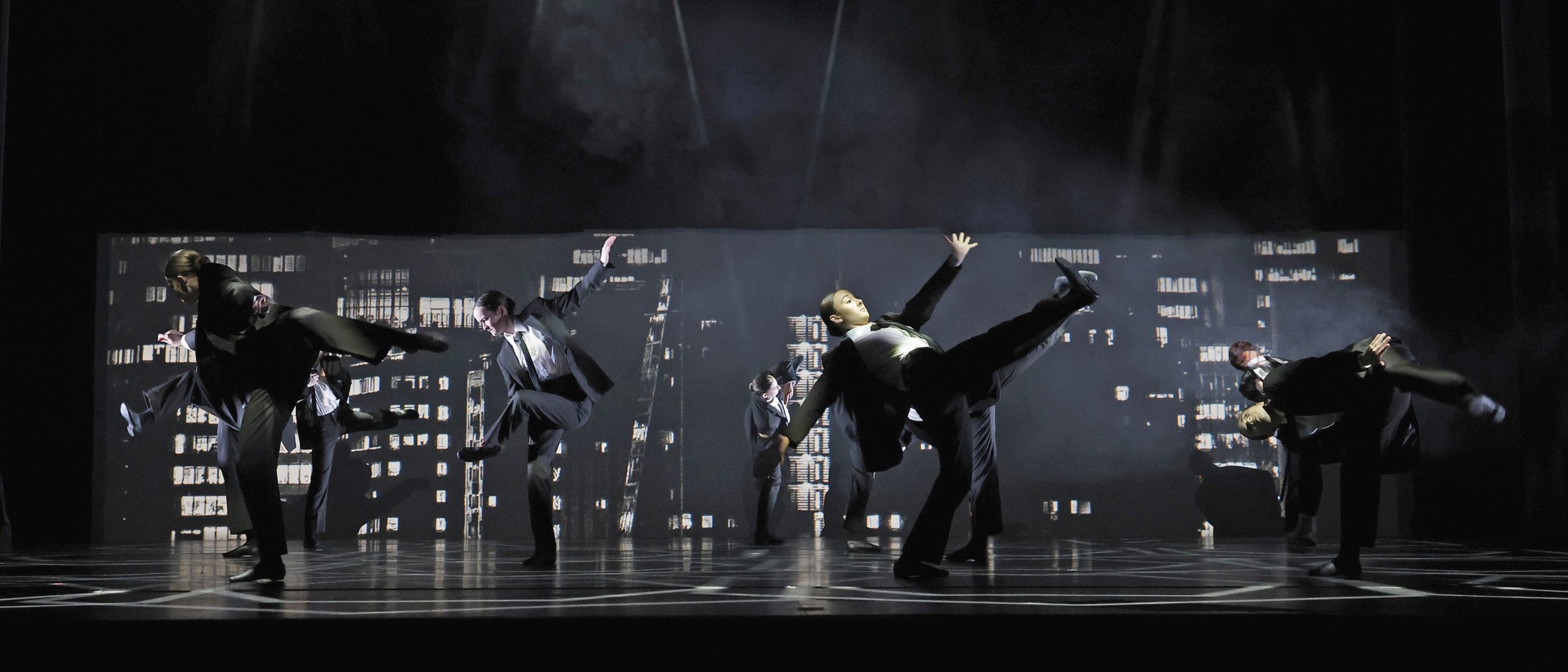 group of dancers in concert on Belk stage, wearing costumes like business suits.