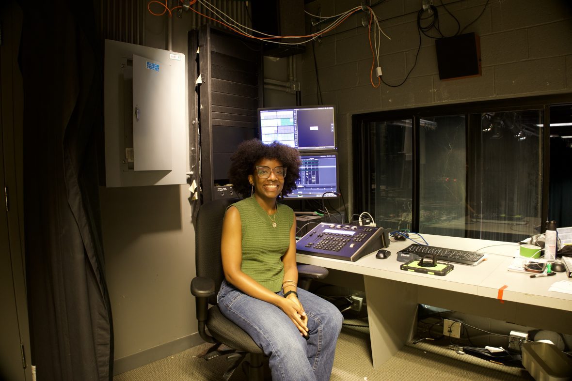Student sitting behind a lighting/sound board and monitor backstage at a production