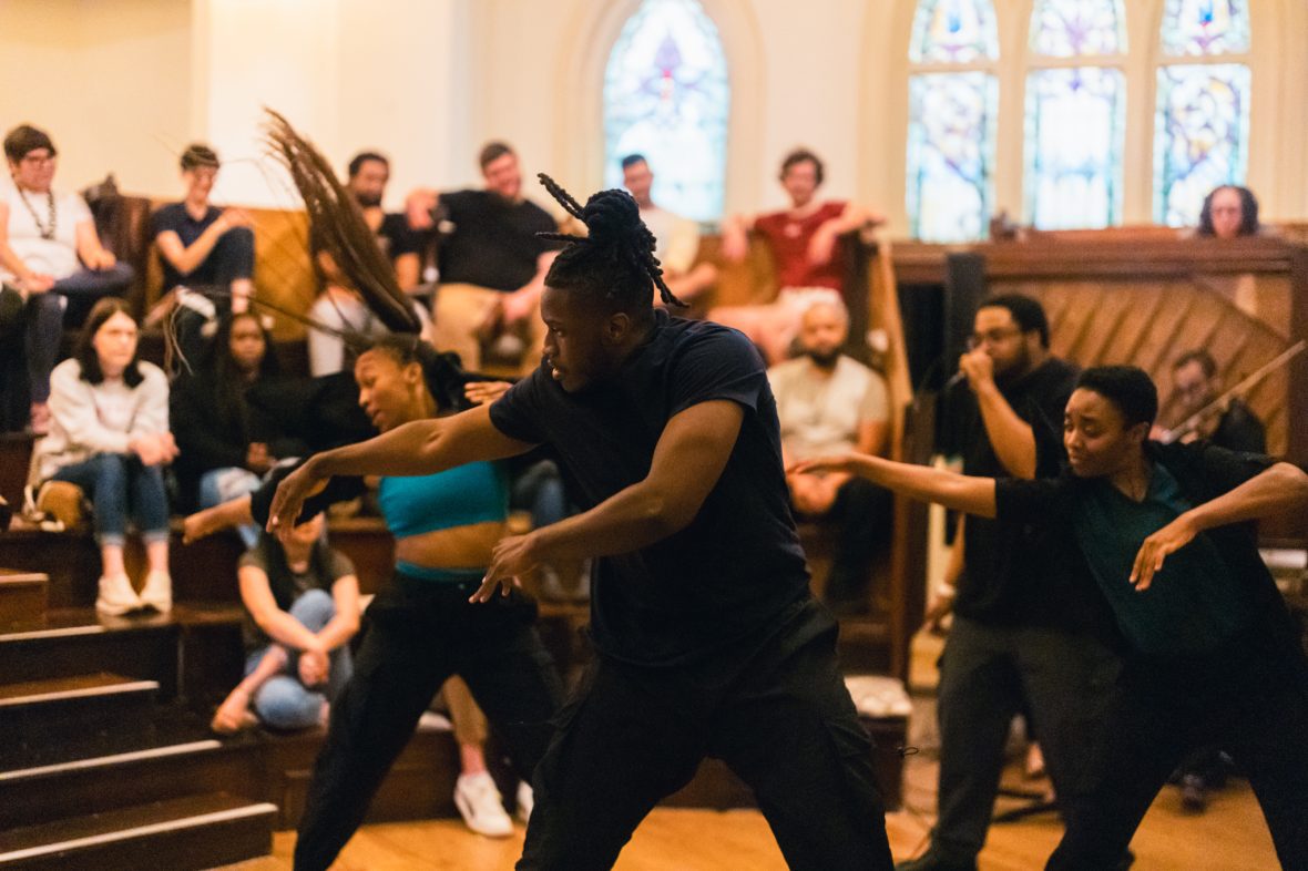 Dancers and vocalist in performance with audience behind them watching