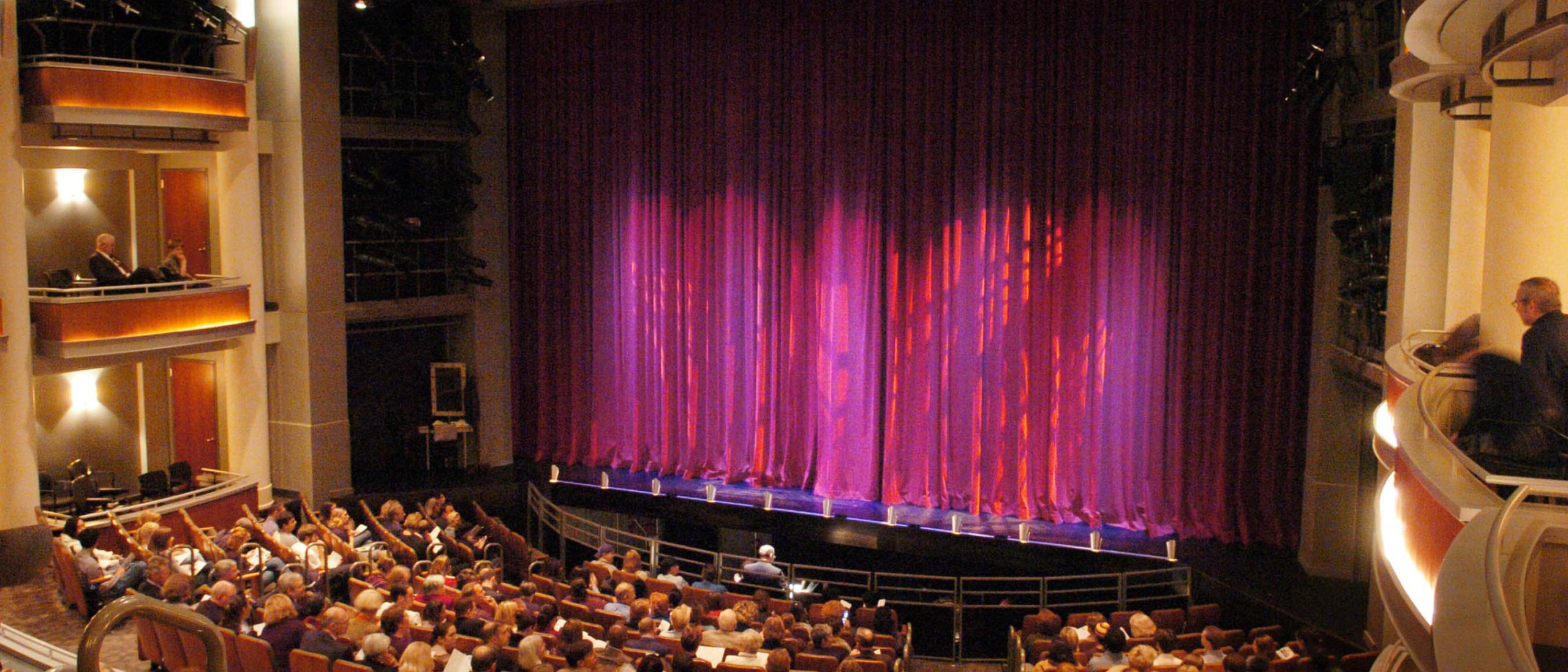 Two dance students, male and female, partnering on stage in red costumes