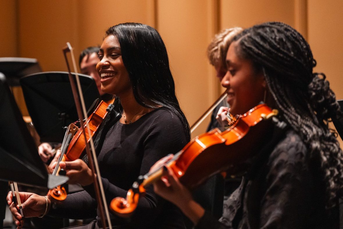 Two female students with violins on stage, smiling
