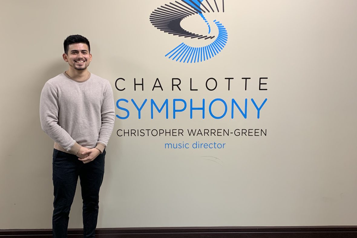 male student in front of the Charlotte Symphony logo at their office for his internship