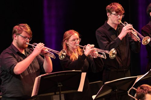 Three students playing trumpets on stage