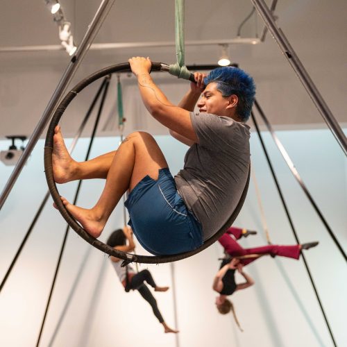 Male student inside an aerial hoop, with two students on trapezes behind