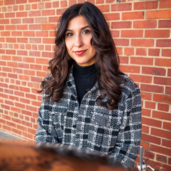 Headshot of Raven Pfeiffer seated at drumset with brick wall behind