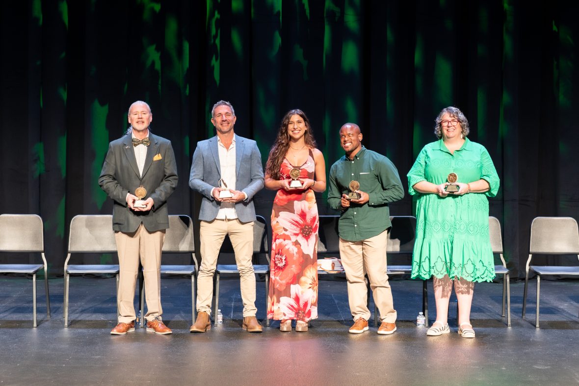 five alumni standing on stage
