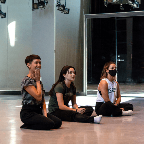 dancers sitting on the floor of a dance studio with their teacher