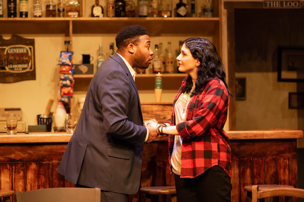 a male and female actor on stage in front of a bar set